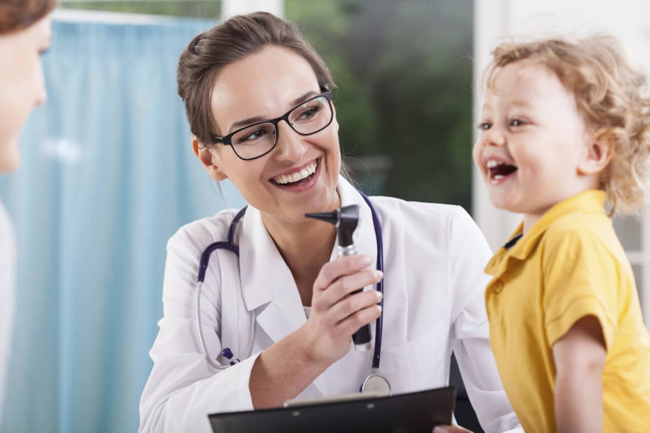Photo of an audiologist holding an otoscope next to a child smiling at another adult