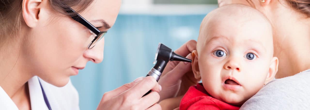 Photo of an audiologist using an otoscope to examine a baby held by another adult