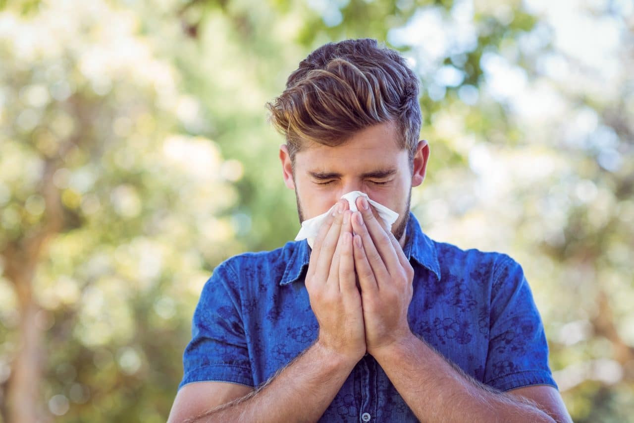 Young man blowing nose outside.