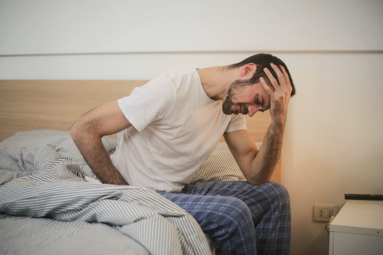 A man with fatigue sitting on the edge of his bed.