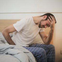 A man with fatigue sitting on the edge of his bed.